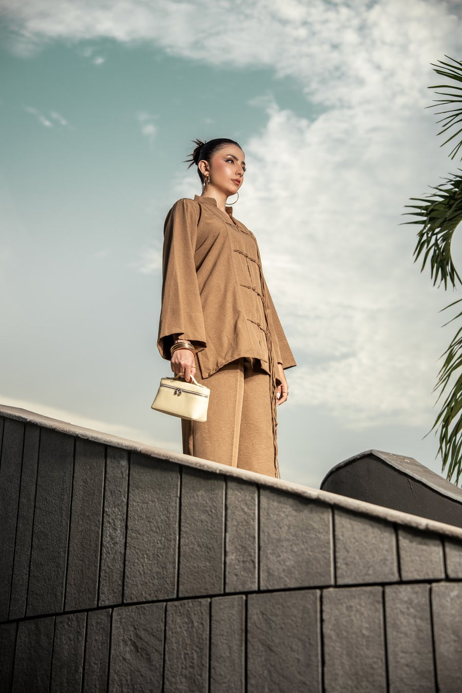A woman in the Dune sand brown co-ord standing against an open sky.